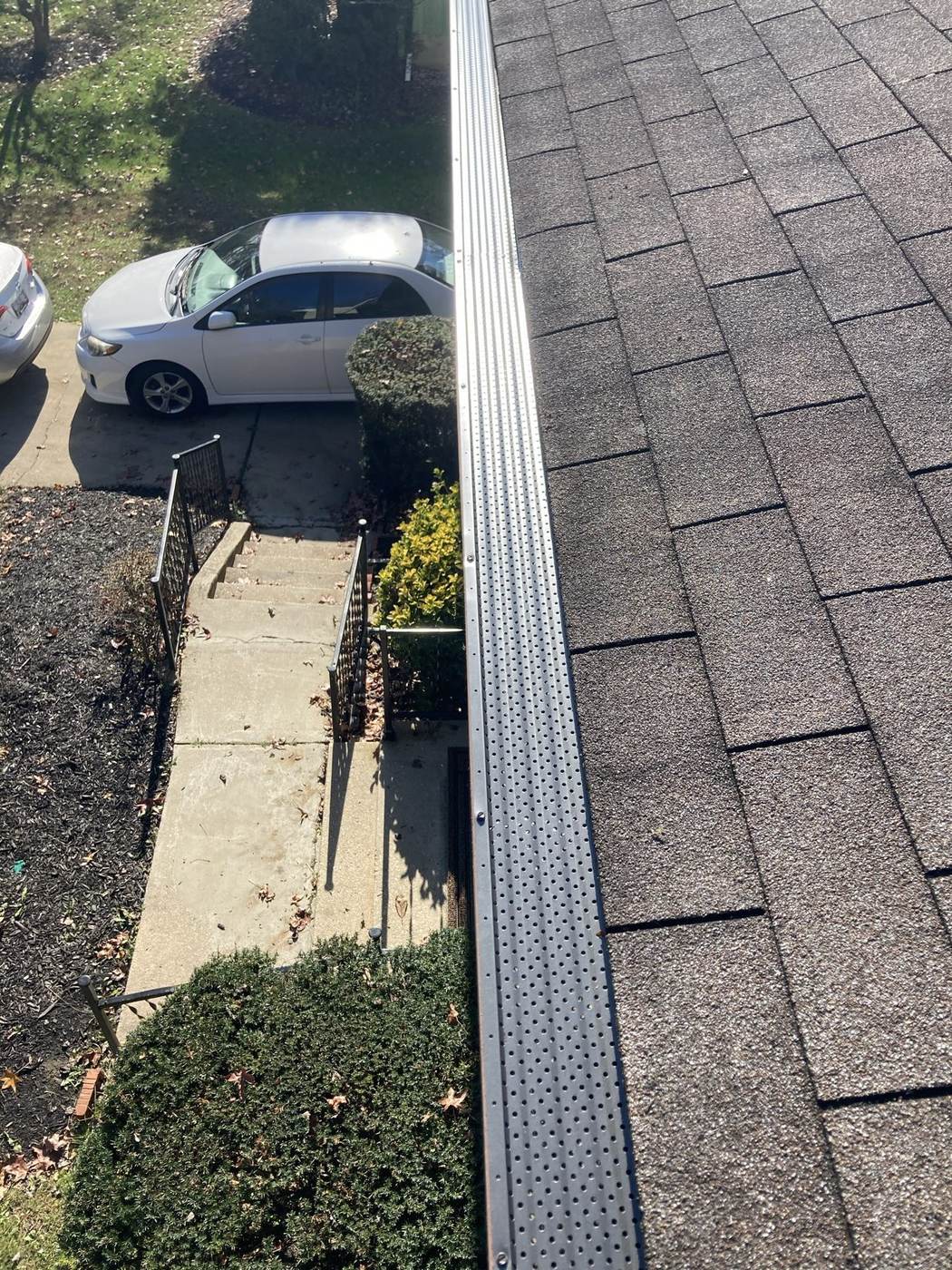 Perforated metal gutter guard installed along a shingle roof edge, viewed from above.