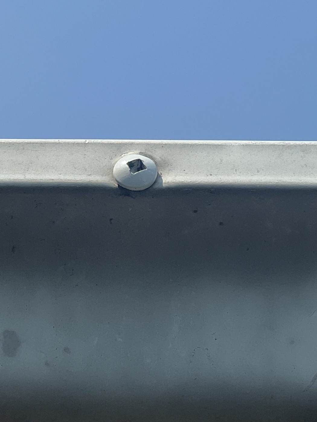 Close-up of a square-drive screw fastening gutter to fascia — modern hangers hold far better than old spike-and-ferrule.