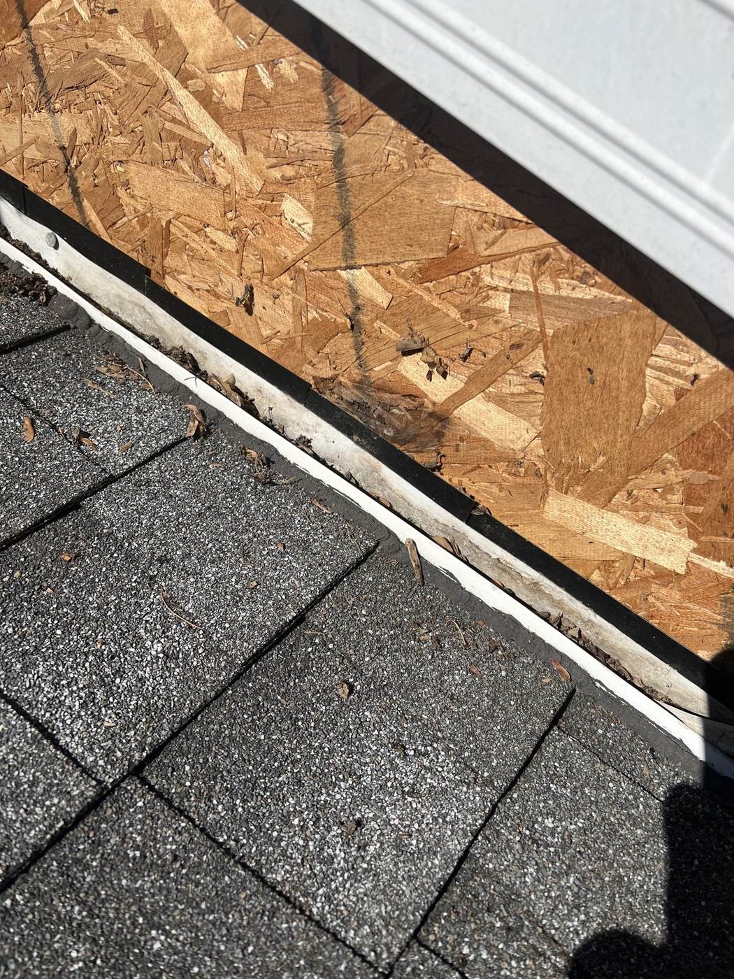 Shingle and flashing repair detail at a stripped wall section, with OSB sheathing exposed.